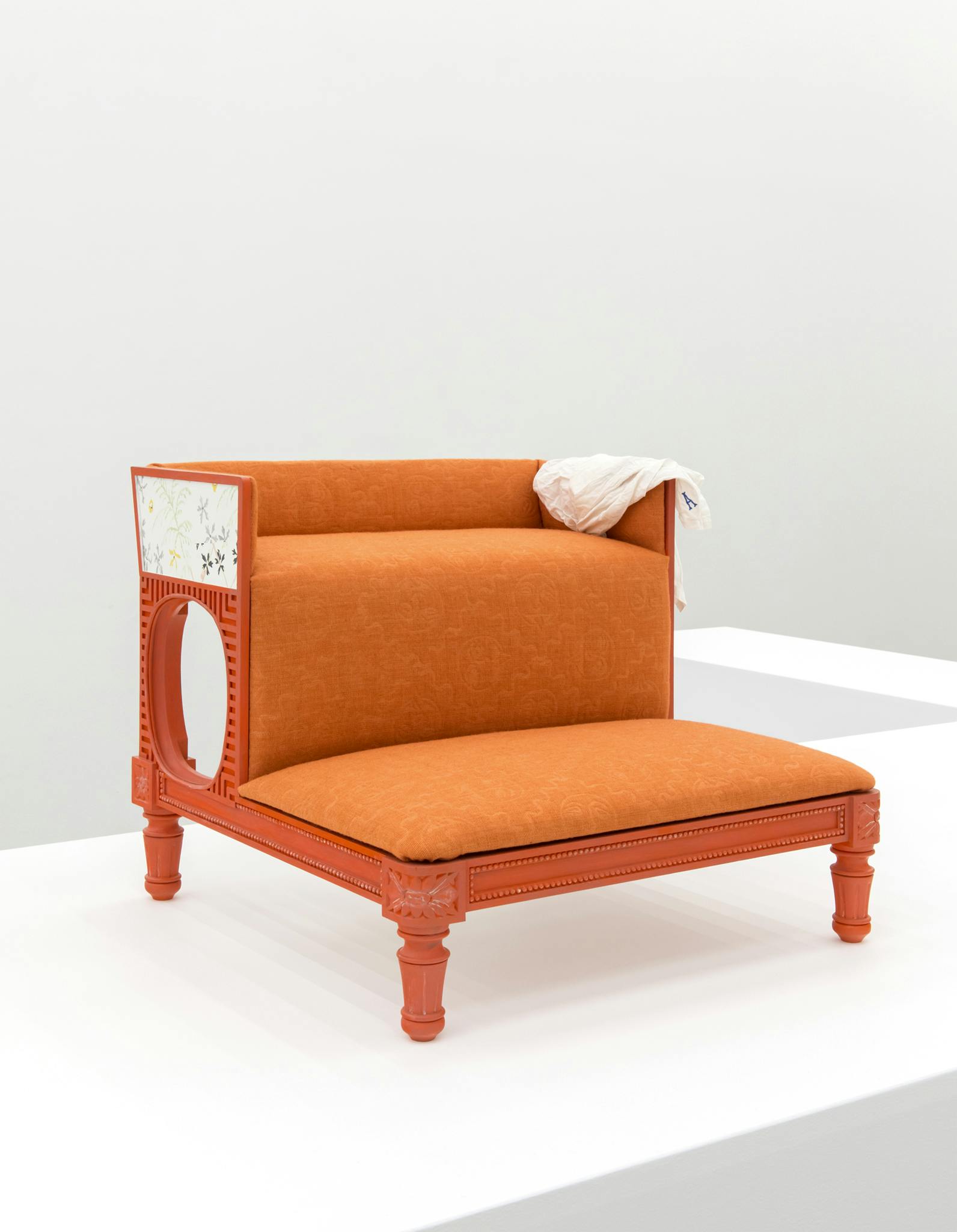An orange bedstep sits on a plinth. Edged in wooden pearl beading, the tread of the steps is upholstered in a hand-dyed and woven, embossed orange fabric.