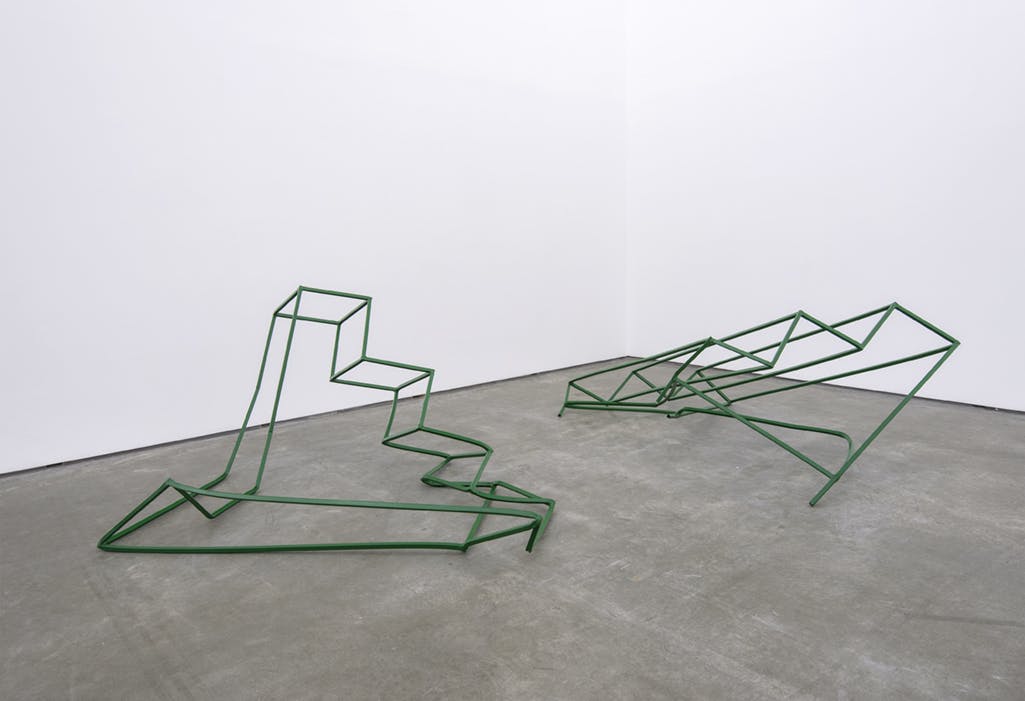 Two free-standing sculptures are placed on the floor. They are made of steel frames and are painted green. The form of both sculptures resembles a distorted staircase.