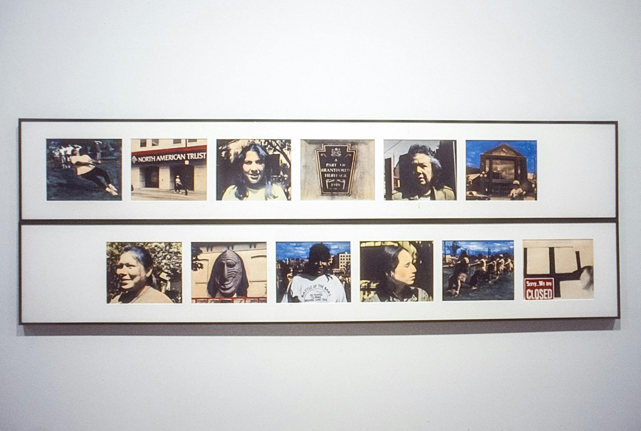 A close-up photo of the artwork mounted on a gallery wall. Two rows of six colored photographs are closely lined up horizontally. Some photographs capture people’s faces, plaques, and road signs.  
