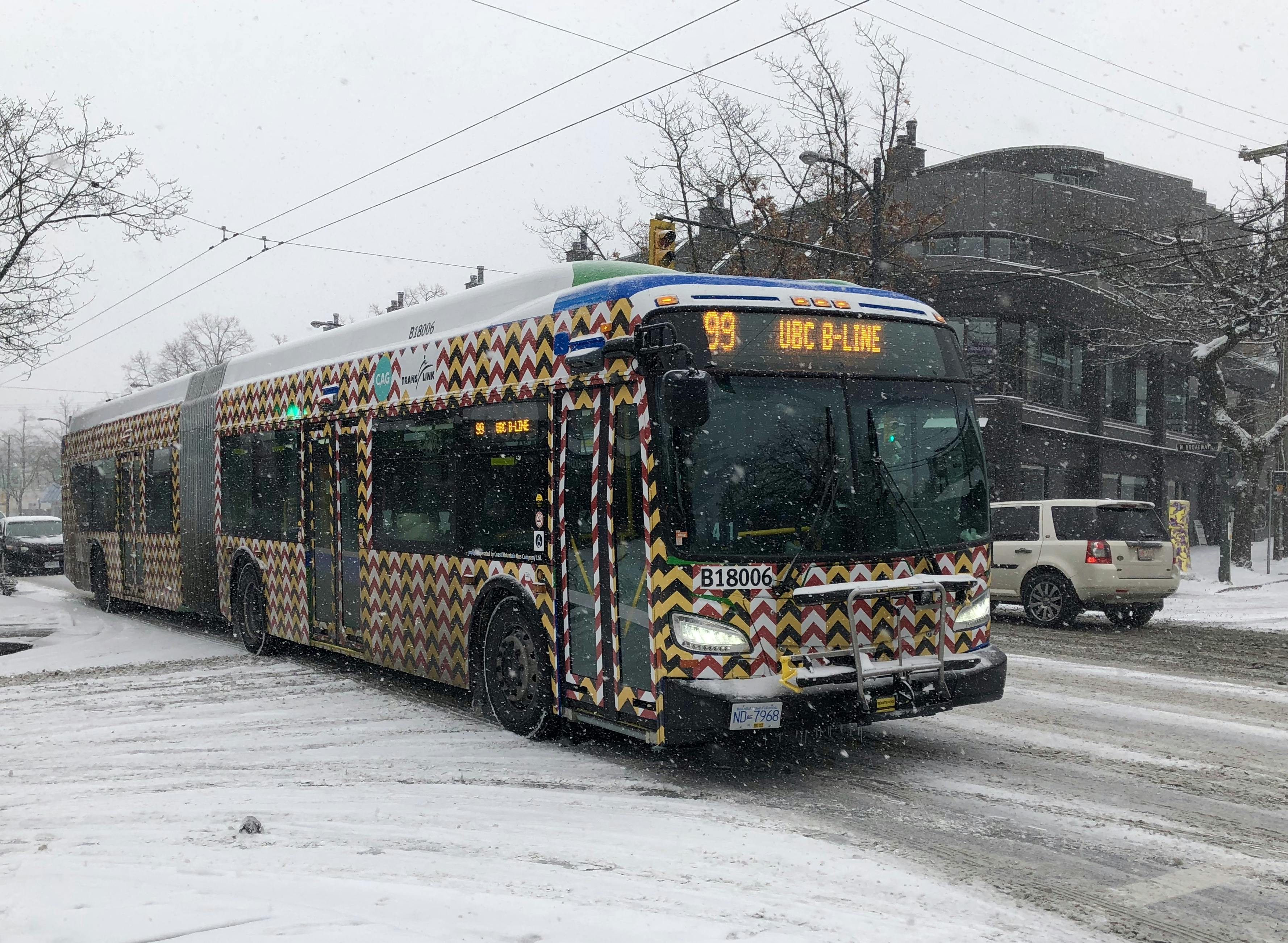 An image of the exterior of a transit bus wrapped in patterned vinyl. The pattern is composed of road work caution tape, with arrow-like shapes alternating from yellow and black to red and white.