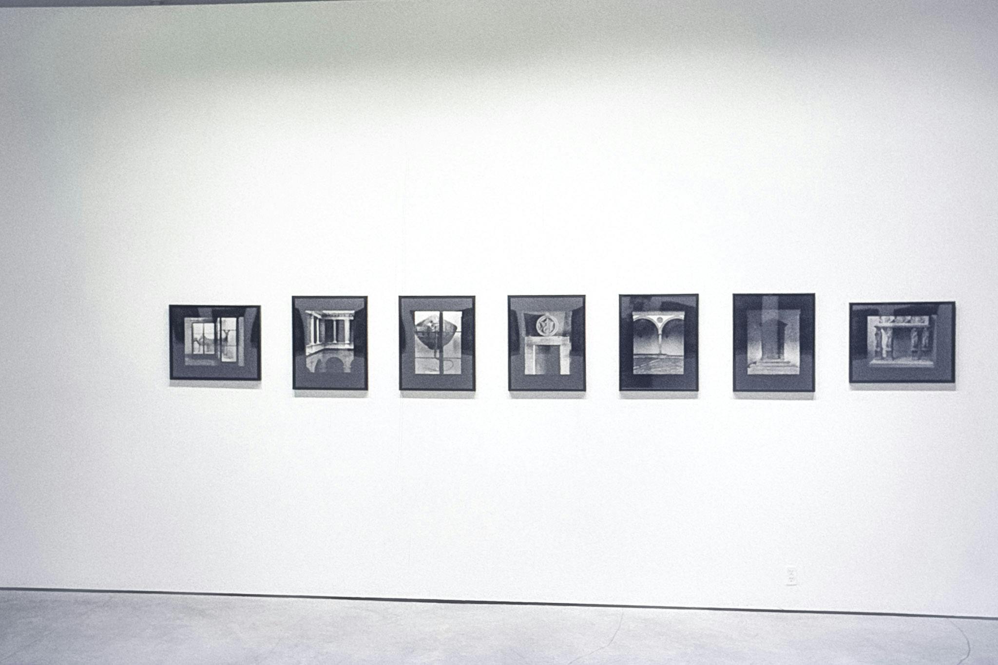 Seven photos in black frames on a wall. All the photos are black and white, showing different arches and doorways. The two photos on the ends are horizontal, and the rest, in the centre, are vertical. 
