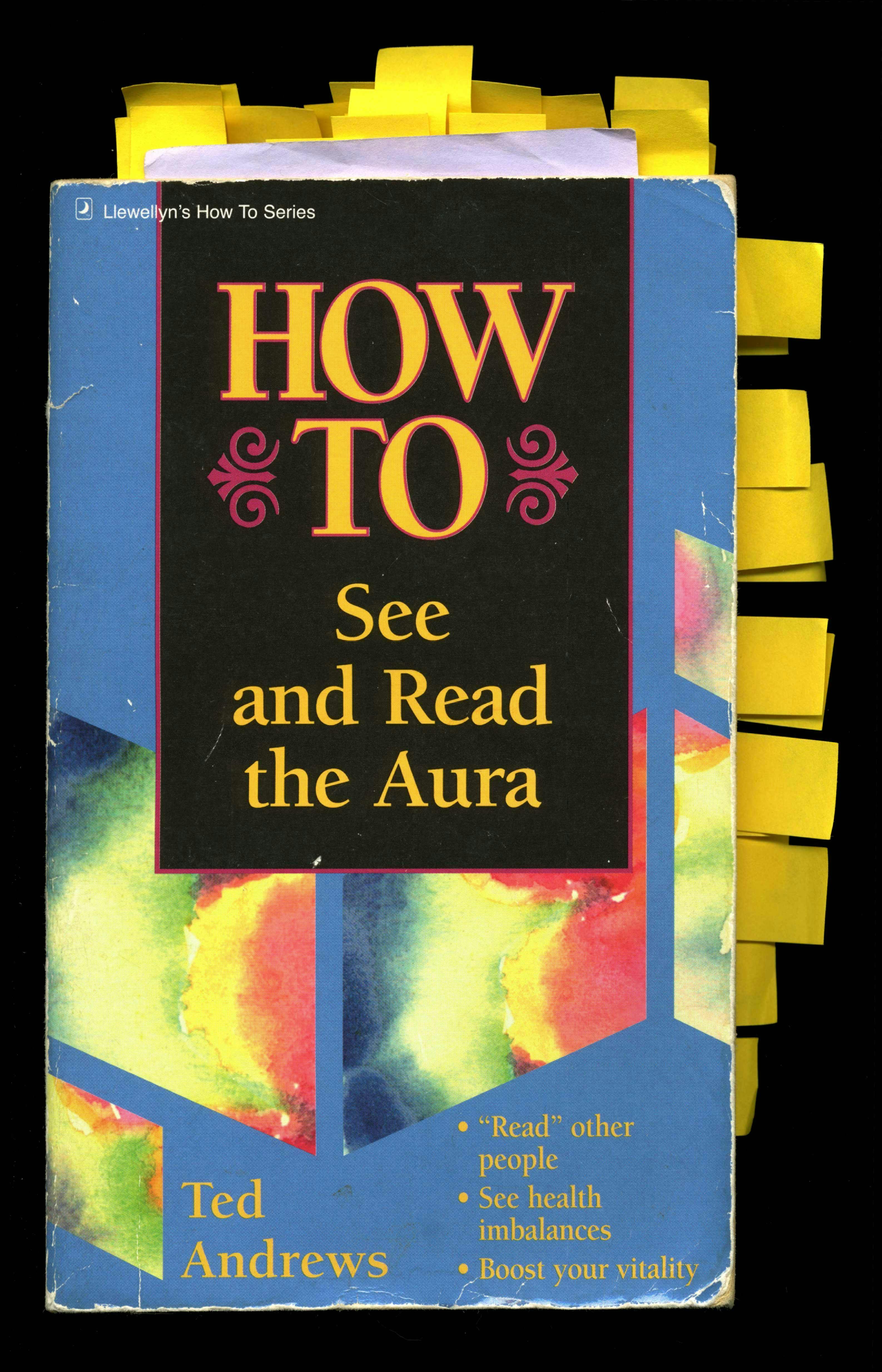An image of the book “HOW TO See and Read the Aura.” The cover is blue with blocks of rainbow coloured patterns and large yellow text. Many tabs of yellow paper stick out from the sides of the book.