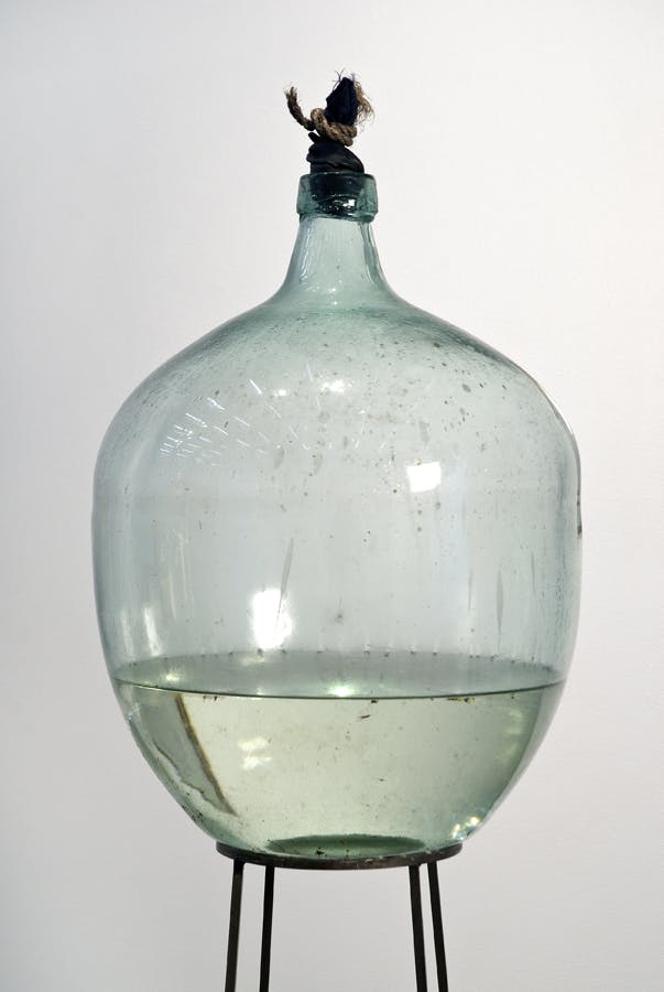 A round glass jug sits on an iron support. Water fills one third of the bottle. 