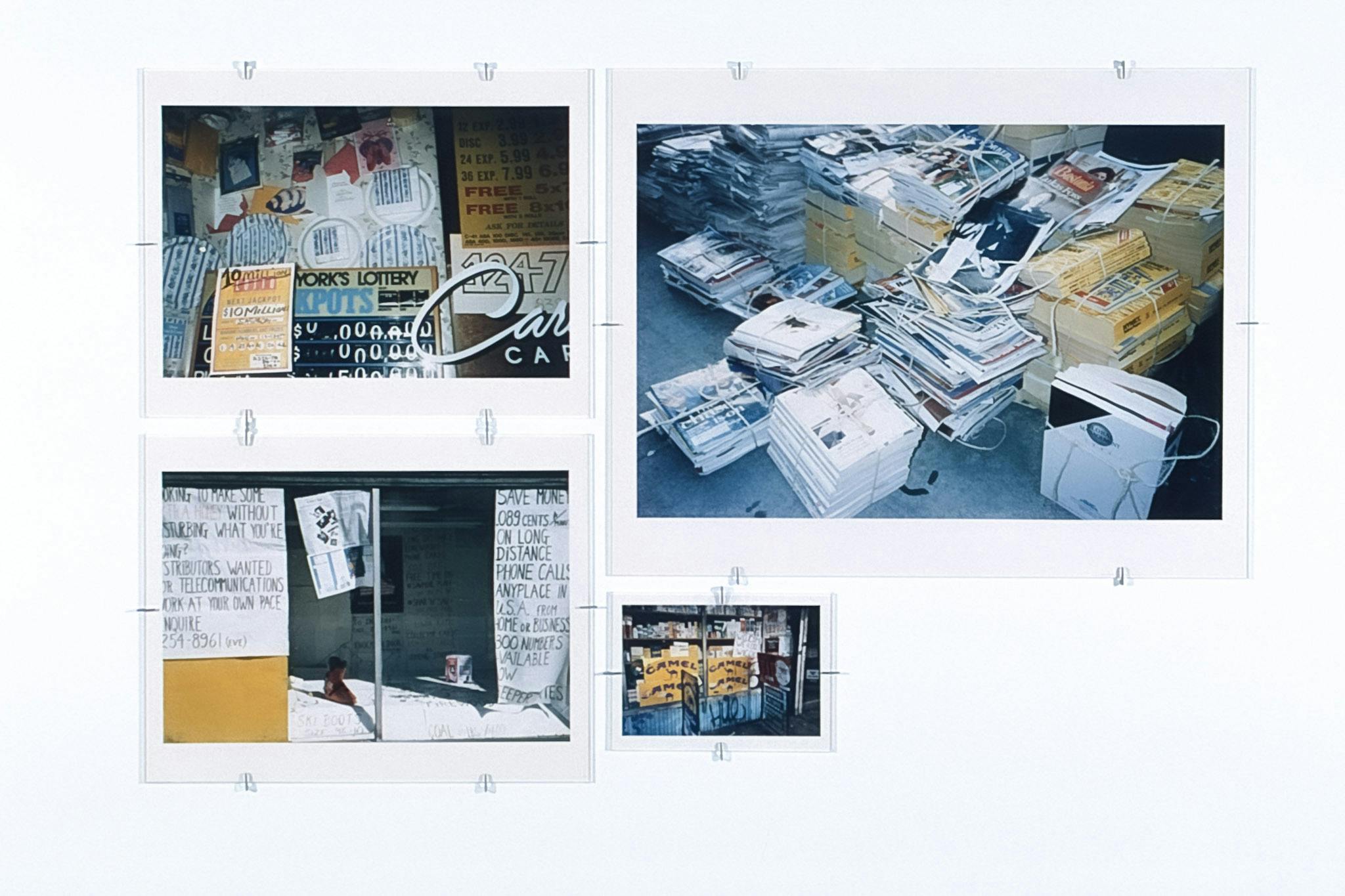 Four coloured photographs of various sizes are displayed on a gallery wall. All images depict paper. One photograph shows signs covering the wall, and the other shows piles of books to be recycled.