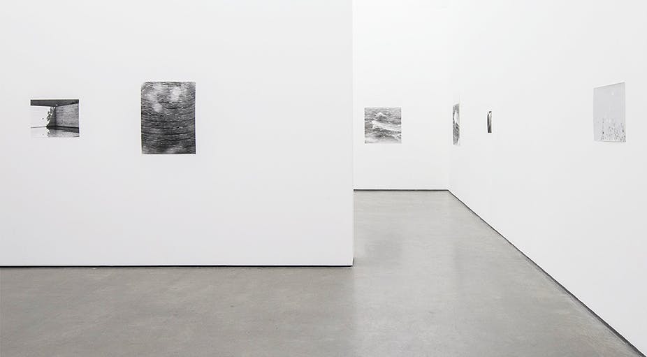 Several black and white photographs are installed on white gallery walls. The photographs look similar with high contrast, low focus compositions.