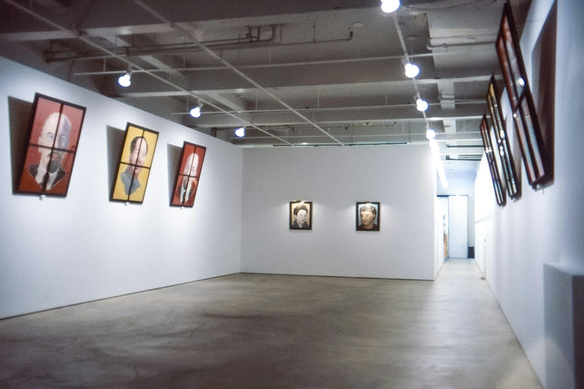 A photo of an installation view in the gallery.  Eight paintings mounted on three walls show the heads of famous historical figures including Mao Zedong and Vladimir Lenin.